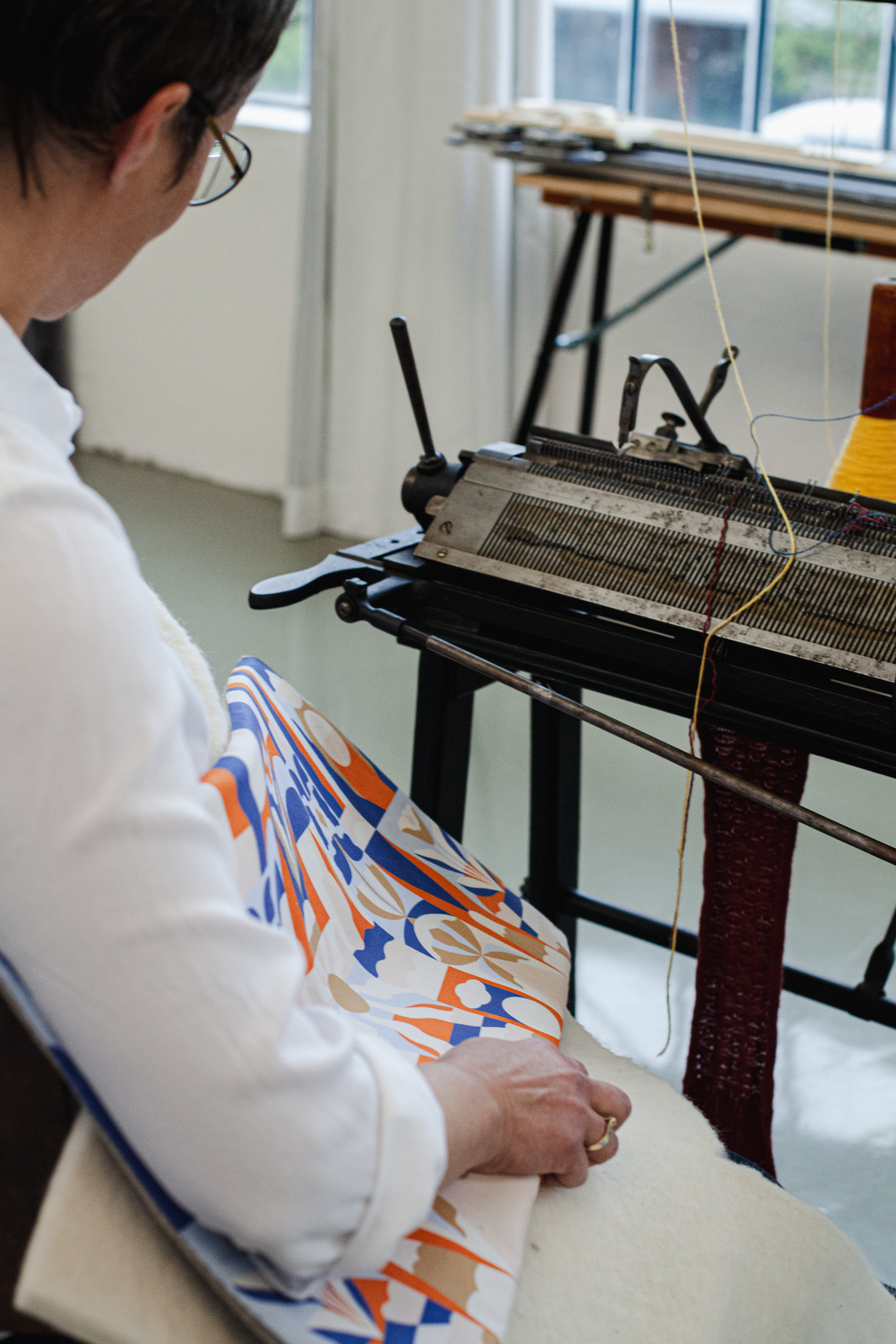 Eine Frau sitzt mit flachem Sitzkissen mit farbigem, geometrischem Muster an alter N&auml;hmaschine.