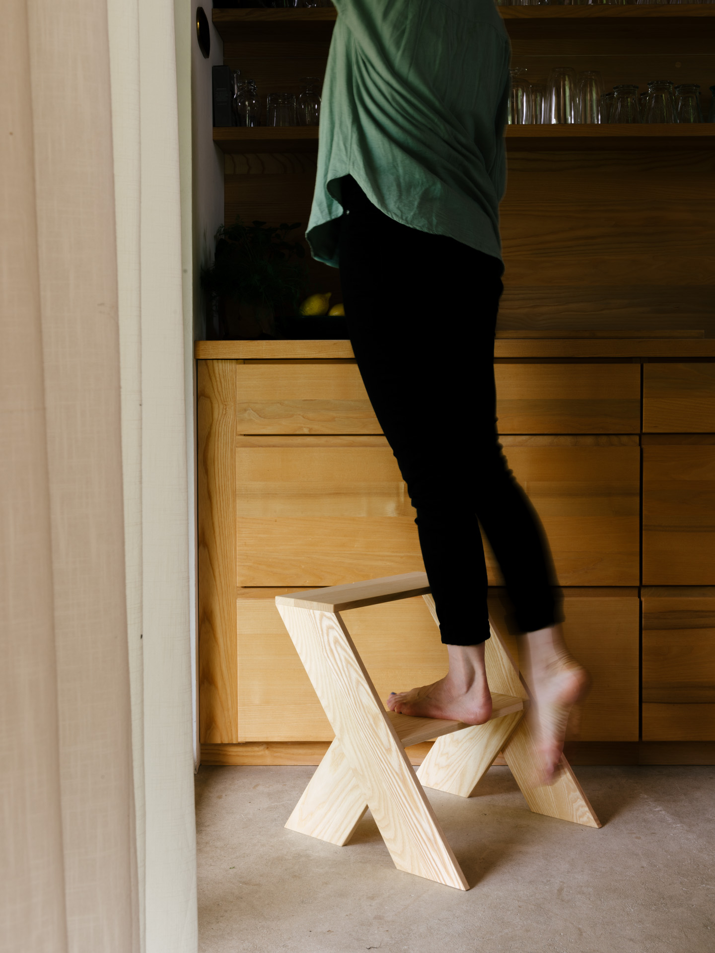 Eine Frau auf einem h&ouml;lzernen Tritthocker an einem K&uuml;chenschrank aus Holz.